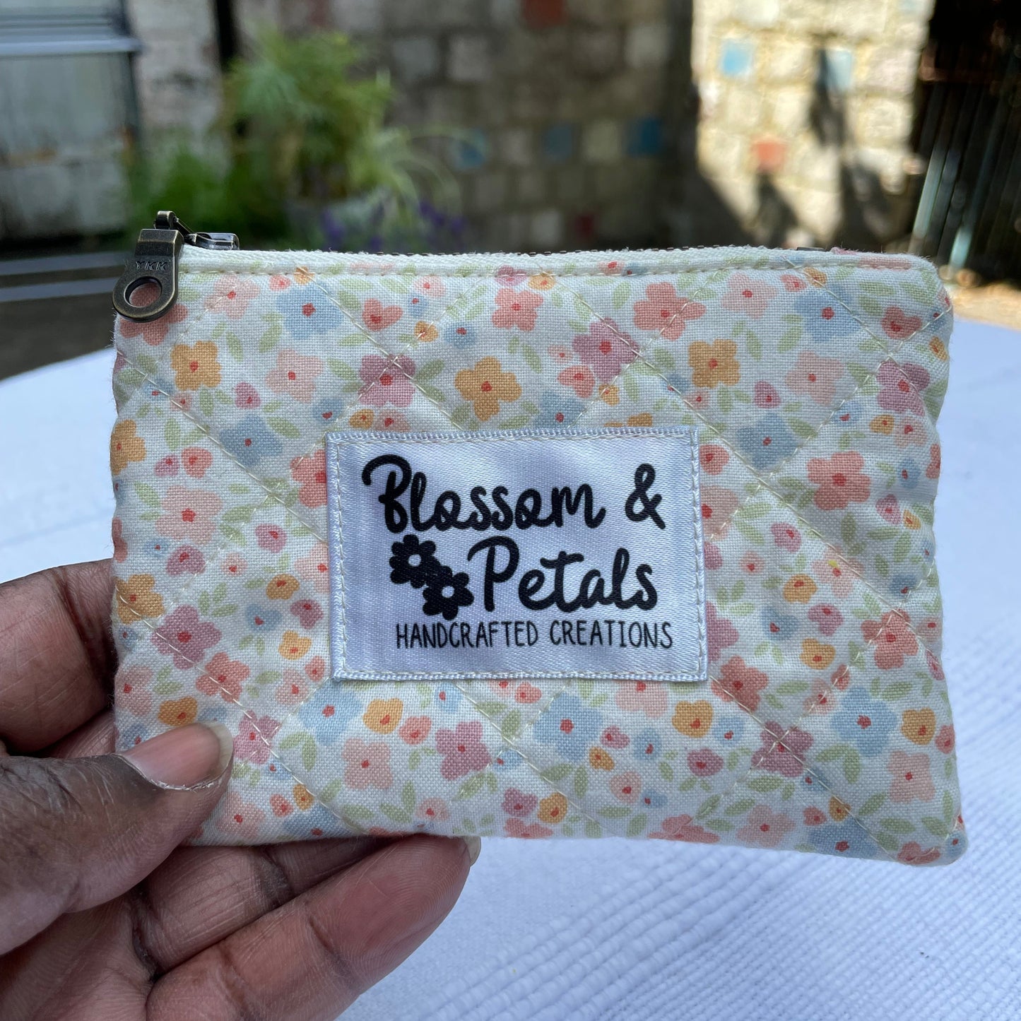 Floral fabric pouch held by a hand with 'Blossom & Petals' label.
