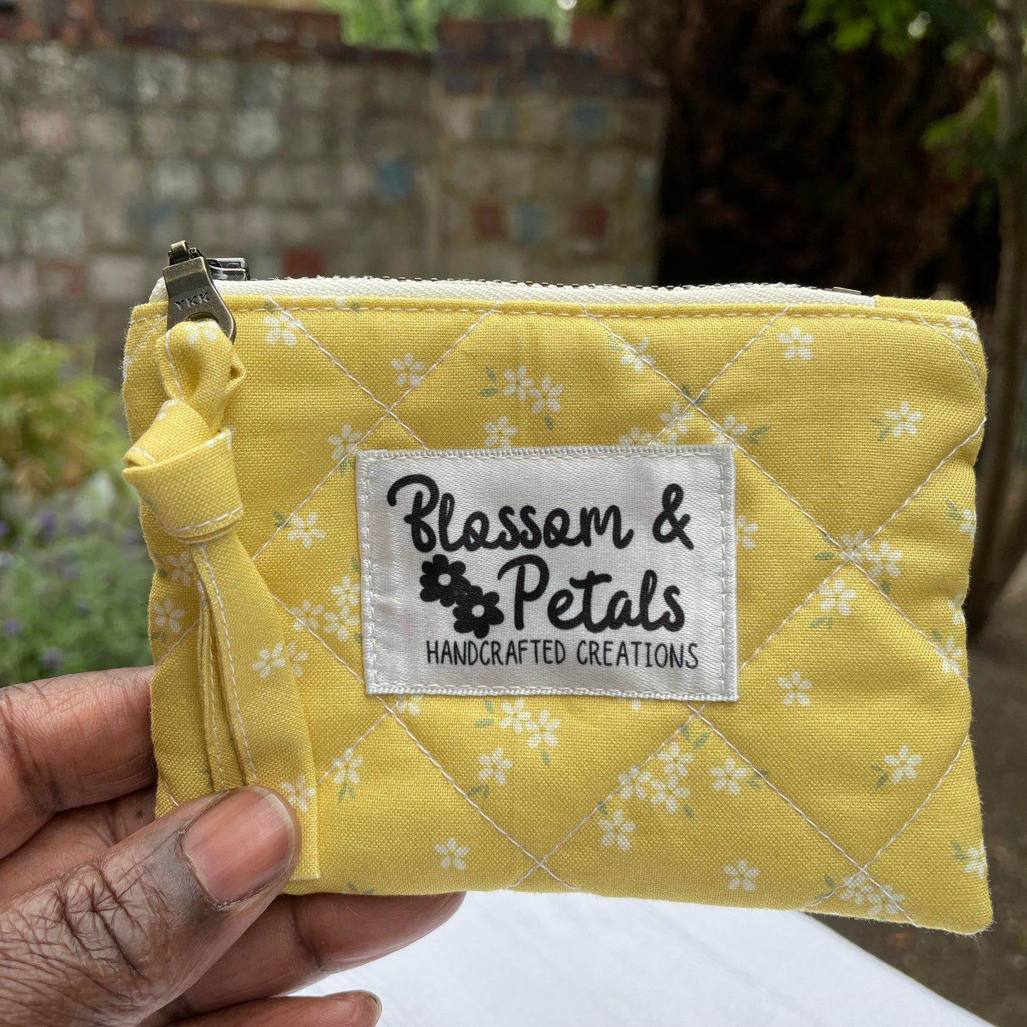 Yellow pouch with floral pattern and 'Blossom & Petals' label held by a hand.