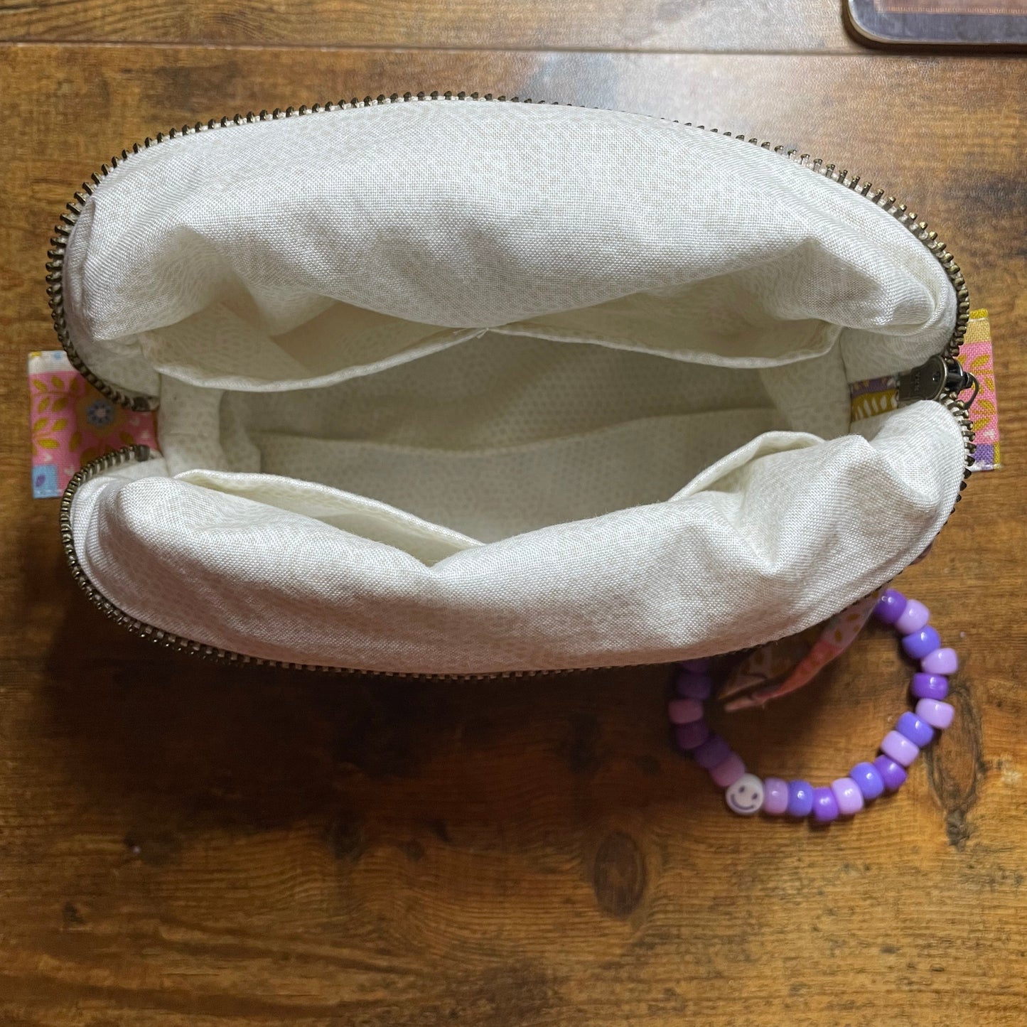 Open quilted patchwork makeup bag on a wooden surface with a purple bracelet on the side