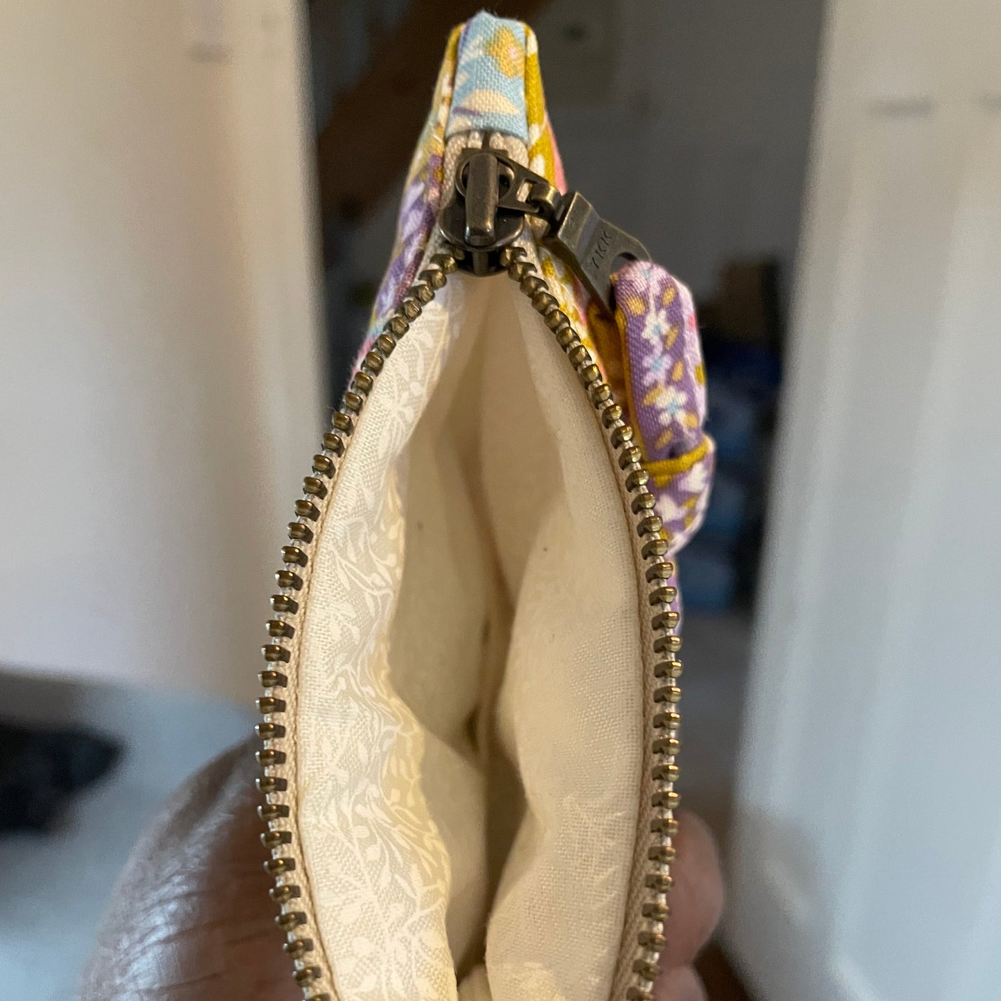 Small pouch with a zipper held open by a hand, showing a patterned exterior.