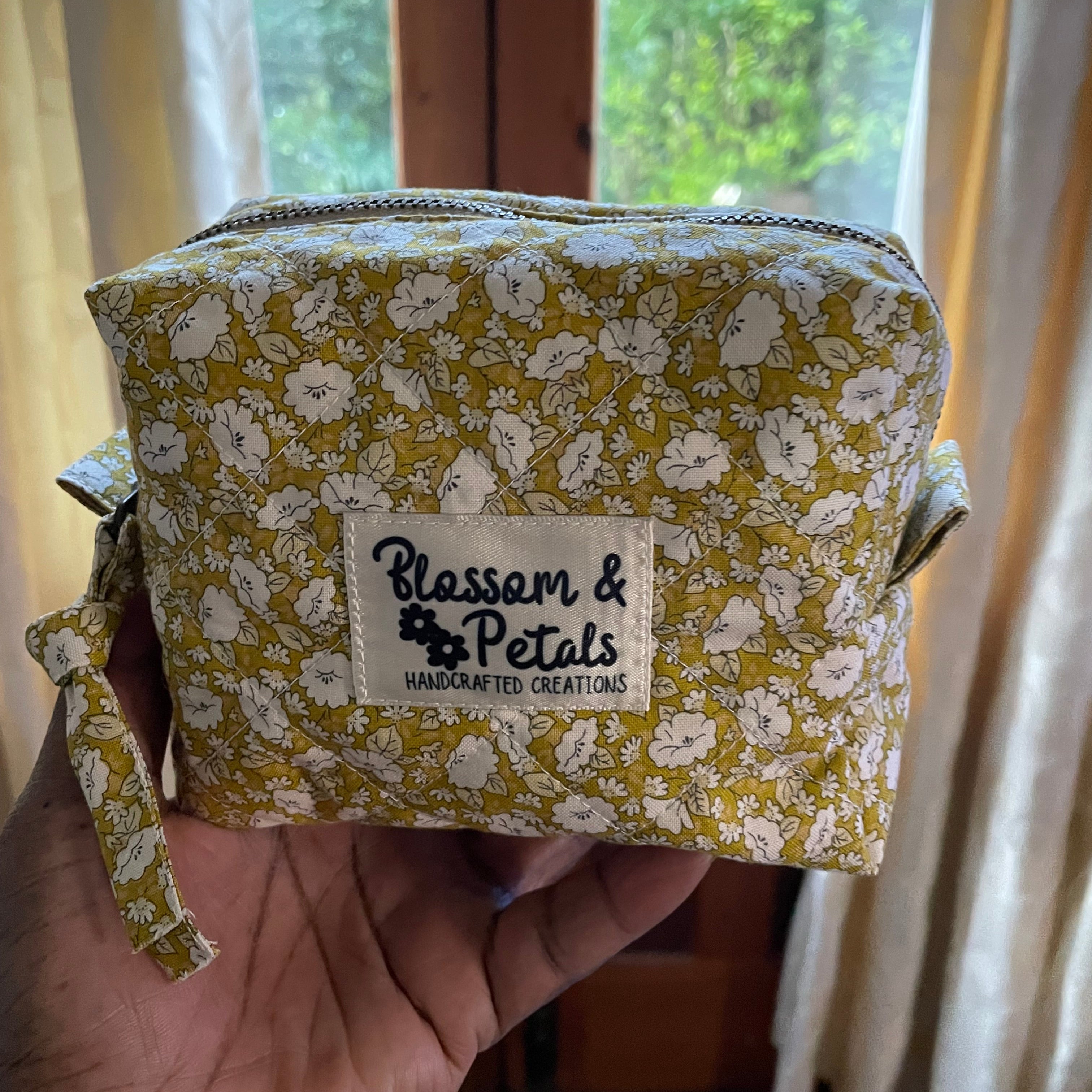 Small fabric pouch with floral pattern and visible brand label held by a hand.