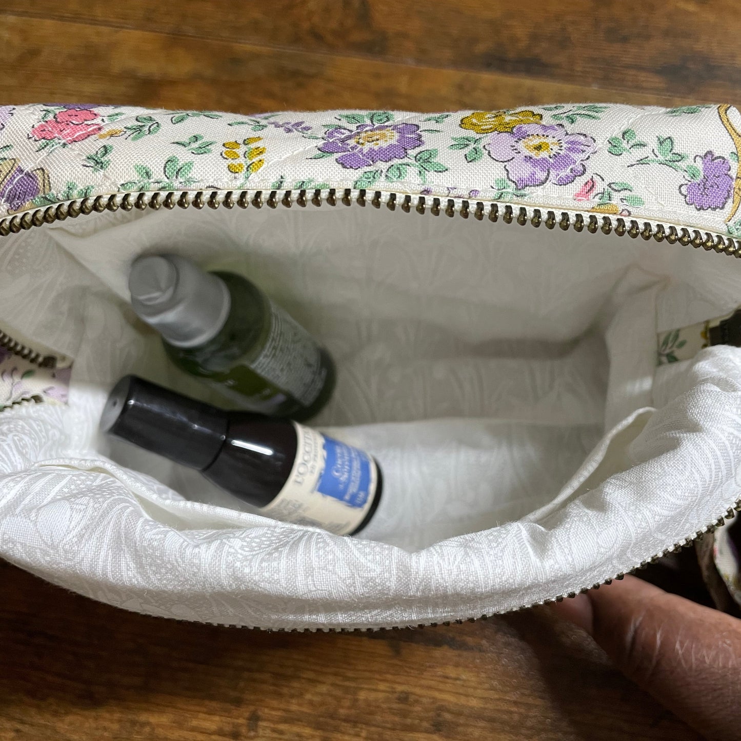 Small floral-patterned pouch with cosmetic items on a wooden surface
