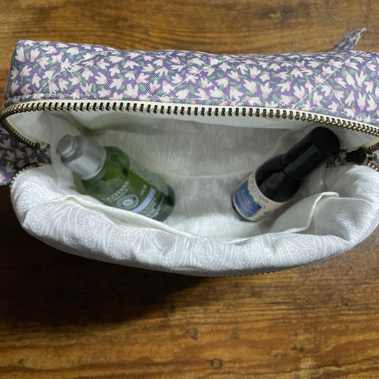 Floral-patterned makeup bag with bottles inside on a wooden surface