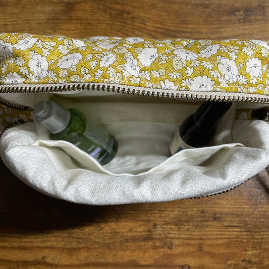Yellow floral-patterned makeup bag with a cream interior, on a wooden surface.