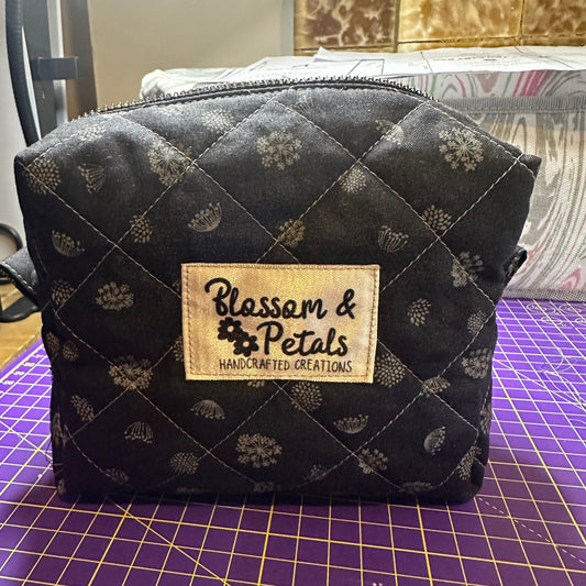 Black quilted pouch with floral pattern and 'Blossom & Petals' label on a purple cutting mat.