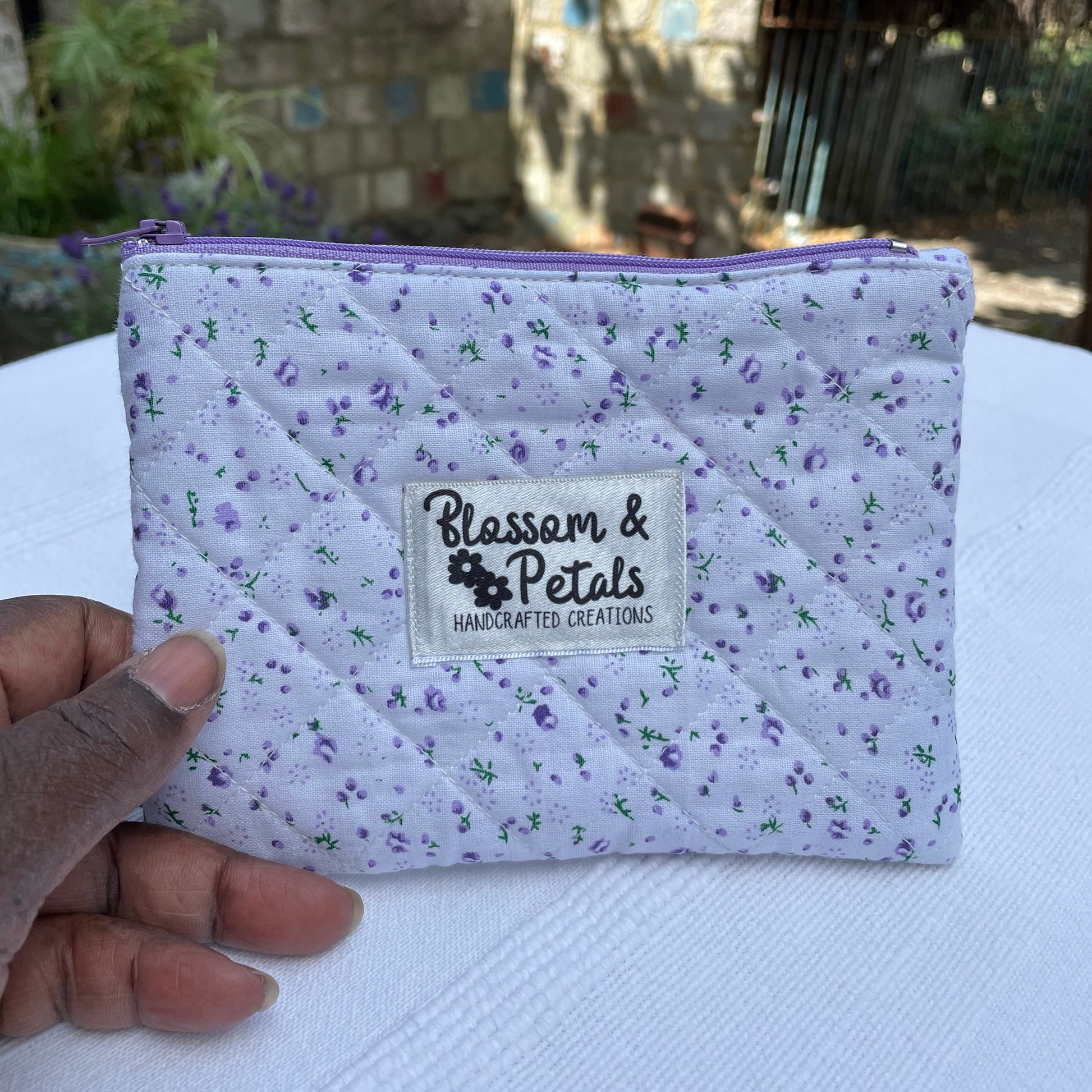 Purple and white quilted pouch with a visible brand label against a blurred background