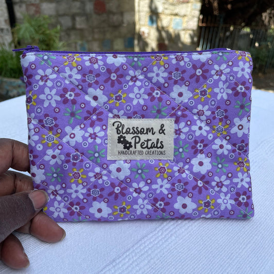 Purple Floral patterned pouch with a visible brand logo held by a hand on a white surface.