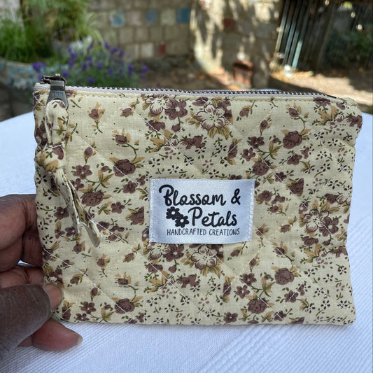 Beige Floral-patterned pouch with a visible brand label held by a hand on a textured surface.