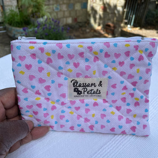 Pink pouch with heart pattern held by a hand, brand 'Blossom & Petals' visible