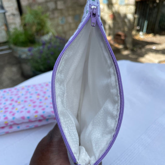 Opened Purple and white pouch show white lining fabric held by a hand with a blurred outdoor background