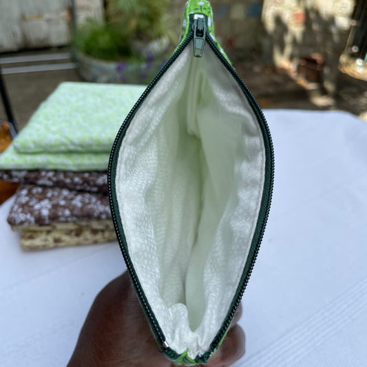 Green pouch with a green zipper held by a hand against a blurred background