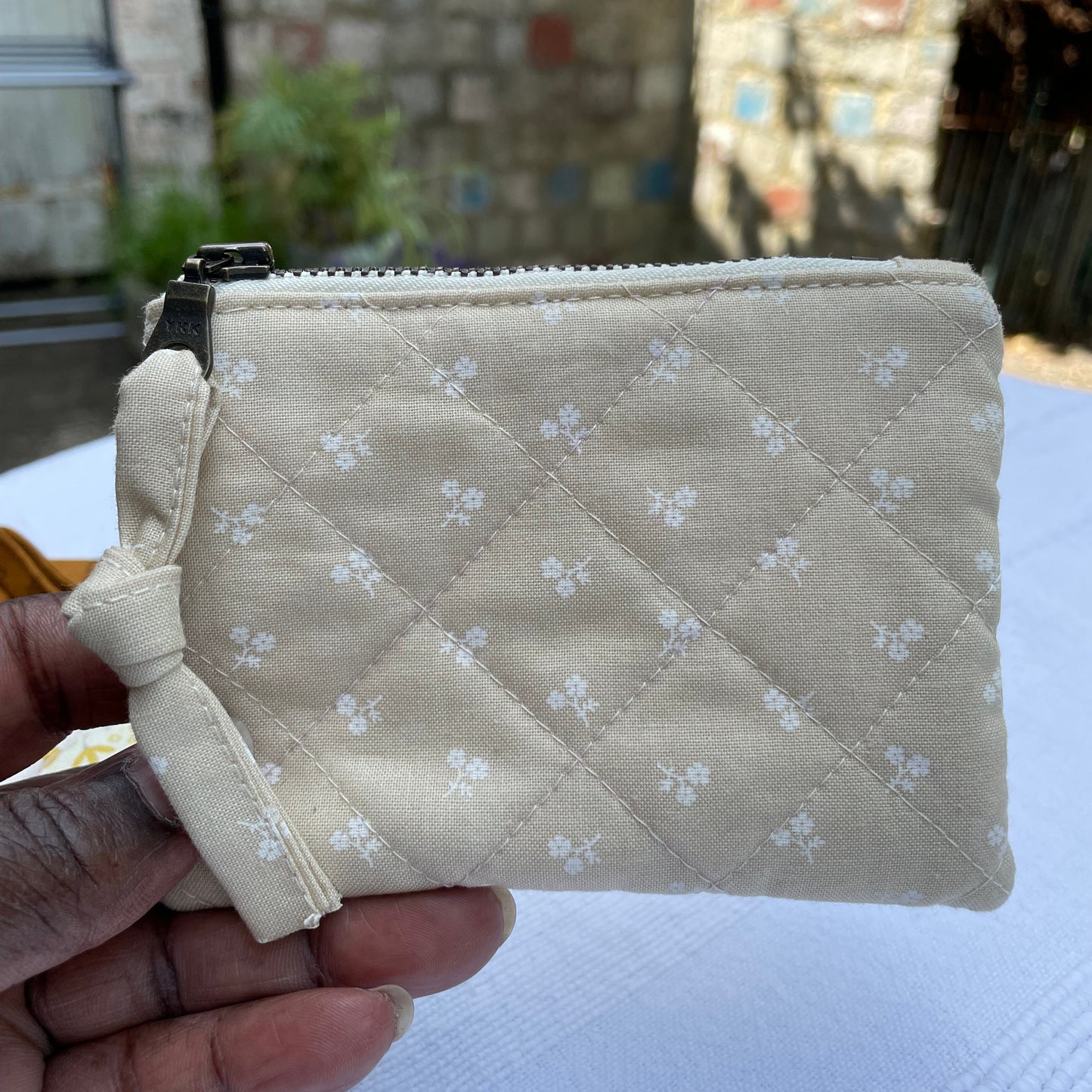 Beige quilted pouch with floral pattern held by a hand against a blurred background