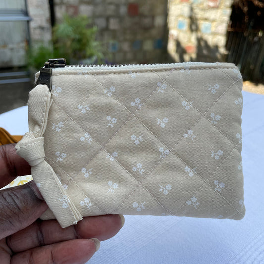 Beige quilted pouch with floral pattern held by a hand against a blurred background