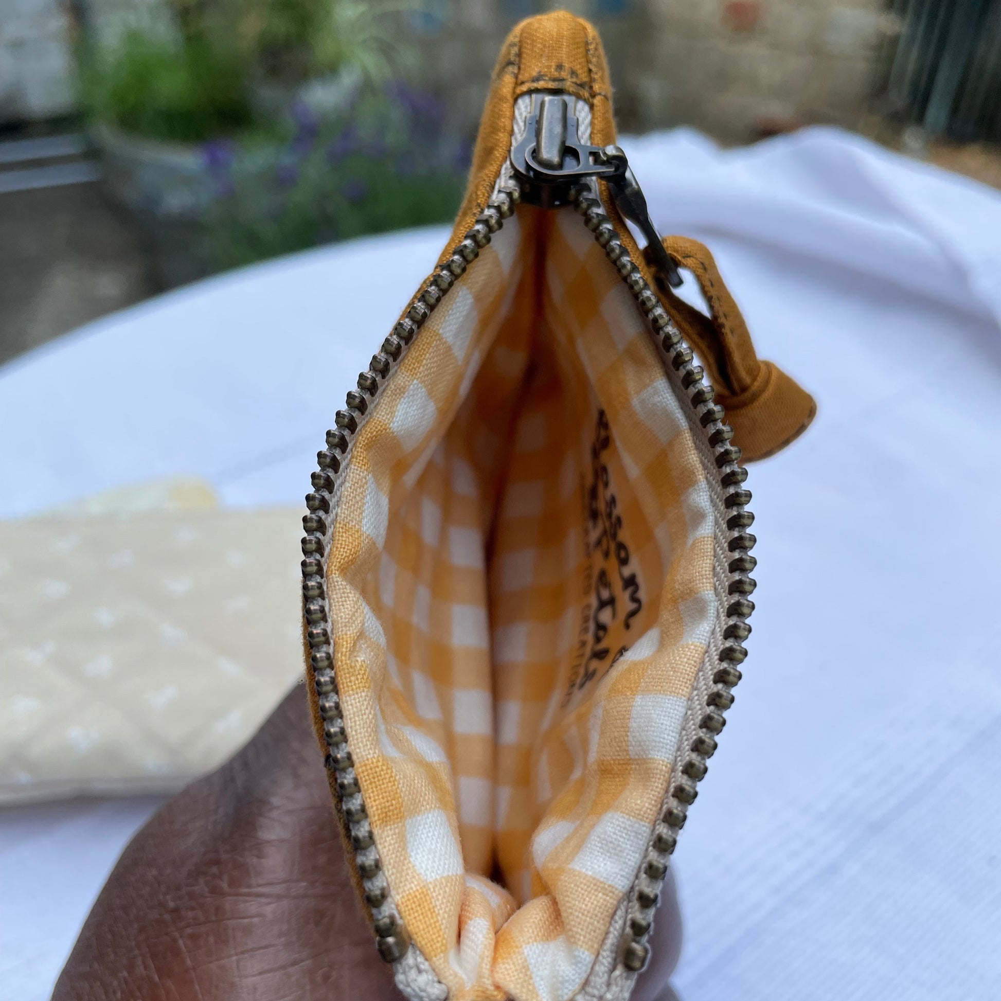 Hand holding a caramel brown with  checkered inner fabric pouch with a zipper.