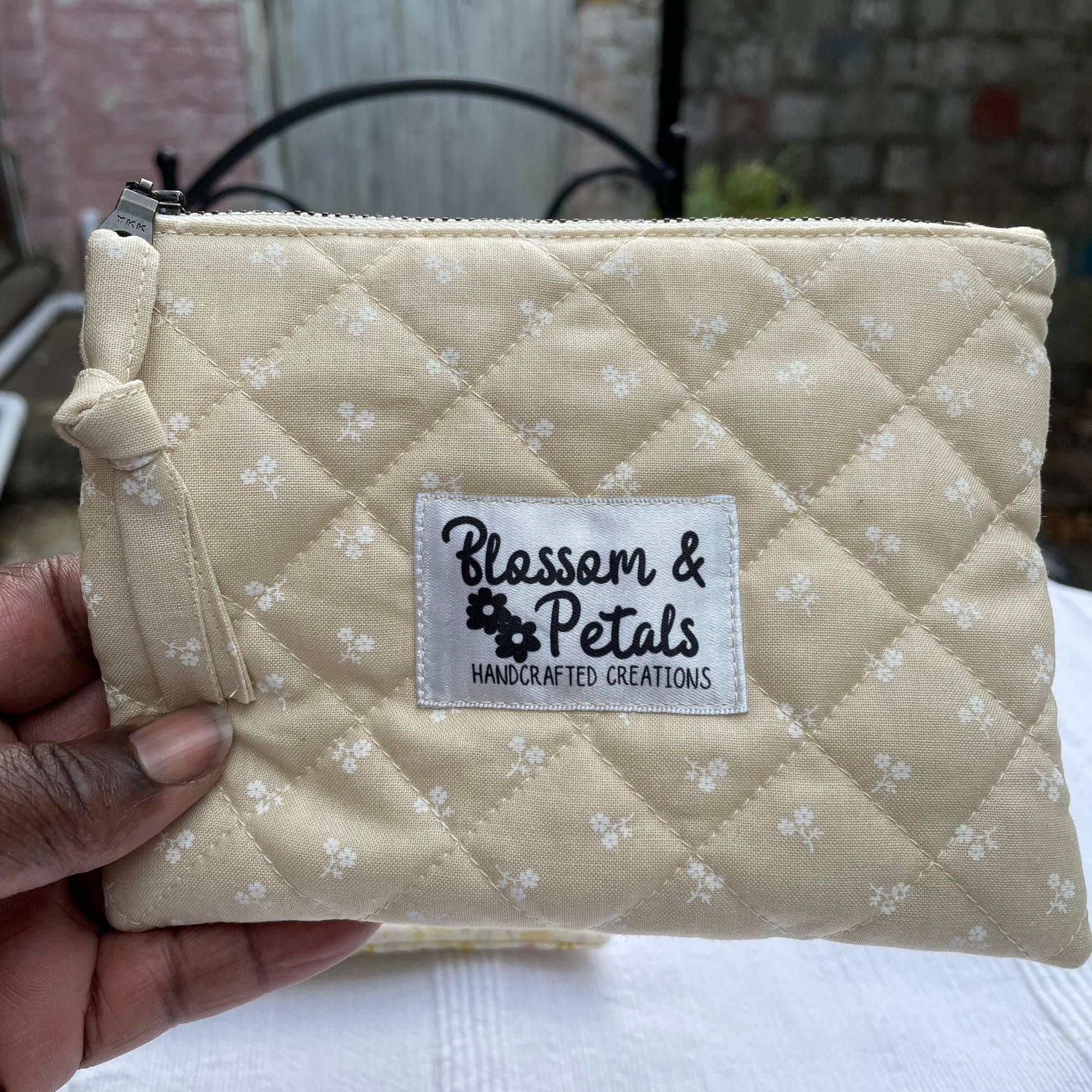 Beige Quilted pouch with floral pattern held by a hand, branded 'Blossoms & Petals'.
