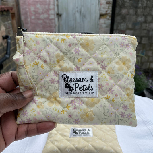 Cream Yellow Floral quilted pouch held by a hand with 'Blossom & Petals' label, rustic background.