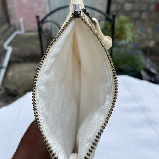 Beige quilted pouch showing white lining with a zipper held by a hand against a blurred background