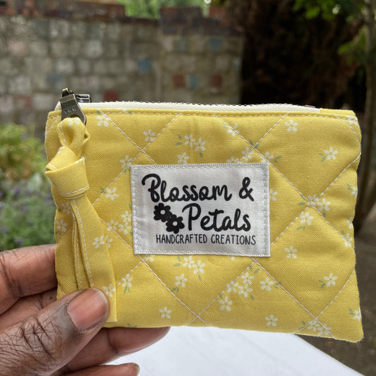 Yellow pouch with floral pattern and 'Blossom & Petals' label held by a hand.