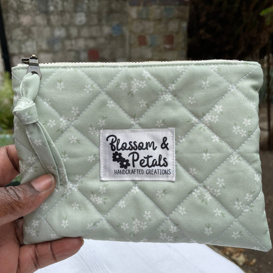 Quilted sage green pouch with floral pattern held by a hand, brand label visible.