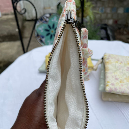 Close-up of a beige pouch with a zipper held by a hand, with a blurred background.