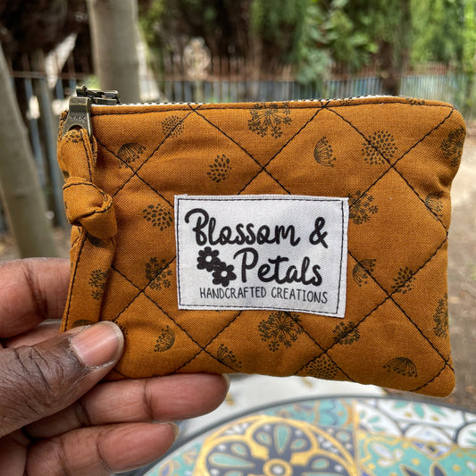 Small quilted pouch with a visible brand label held by a hand, with a decorative background.