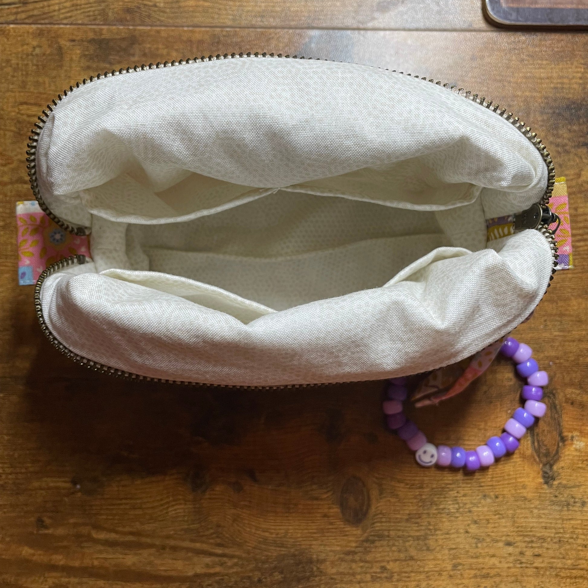 Open quilted patchwork makeup bag on a wooden surface with a purple bracelet on the side