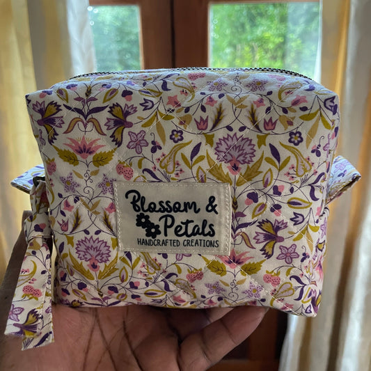 Handmade quilted pouch with cream background and purple floral print, displayed in hand with Blossom & Petals branding