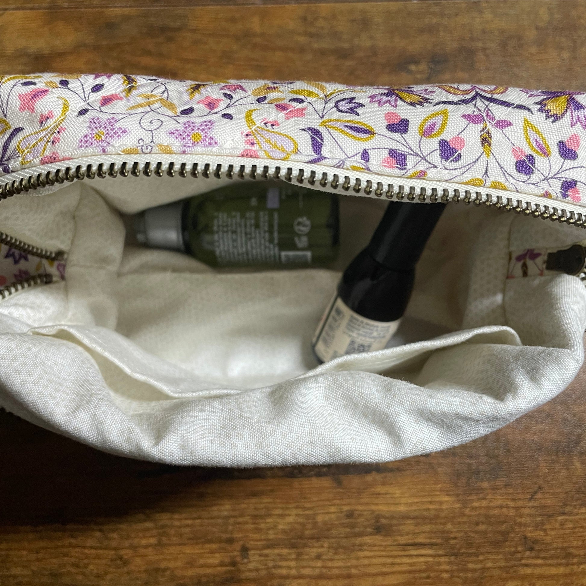 Floral-patterned makeup bag with a bottle of hand sanitizer on a wooden surface
