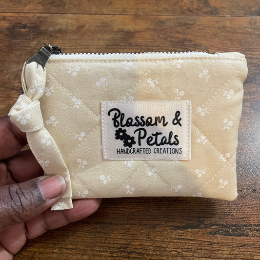 Beige pouch with floral pattern held by a hand on a wooden surface, featuring 'Blossoms & Petals' label.