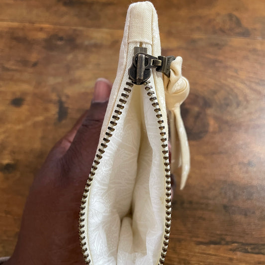 Hand holding a beige zipper pouch against a wooden background
