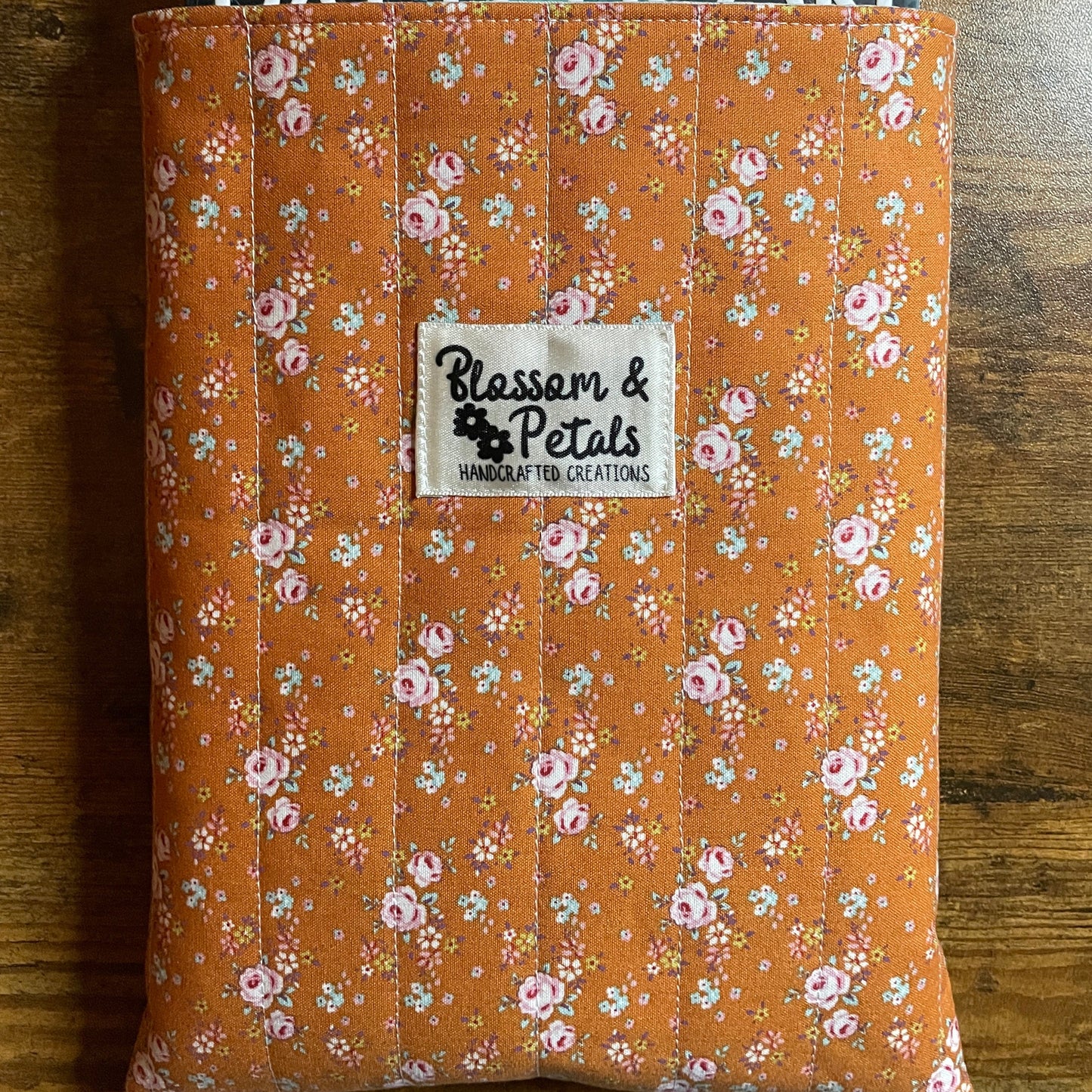 Handmade quilted book sleeve in rust floral cotton fabric with padded design to protect books, journals, planners, and e-readers.