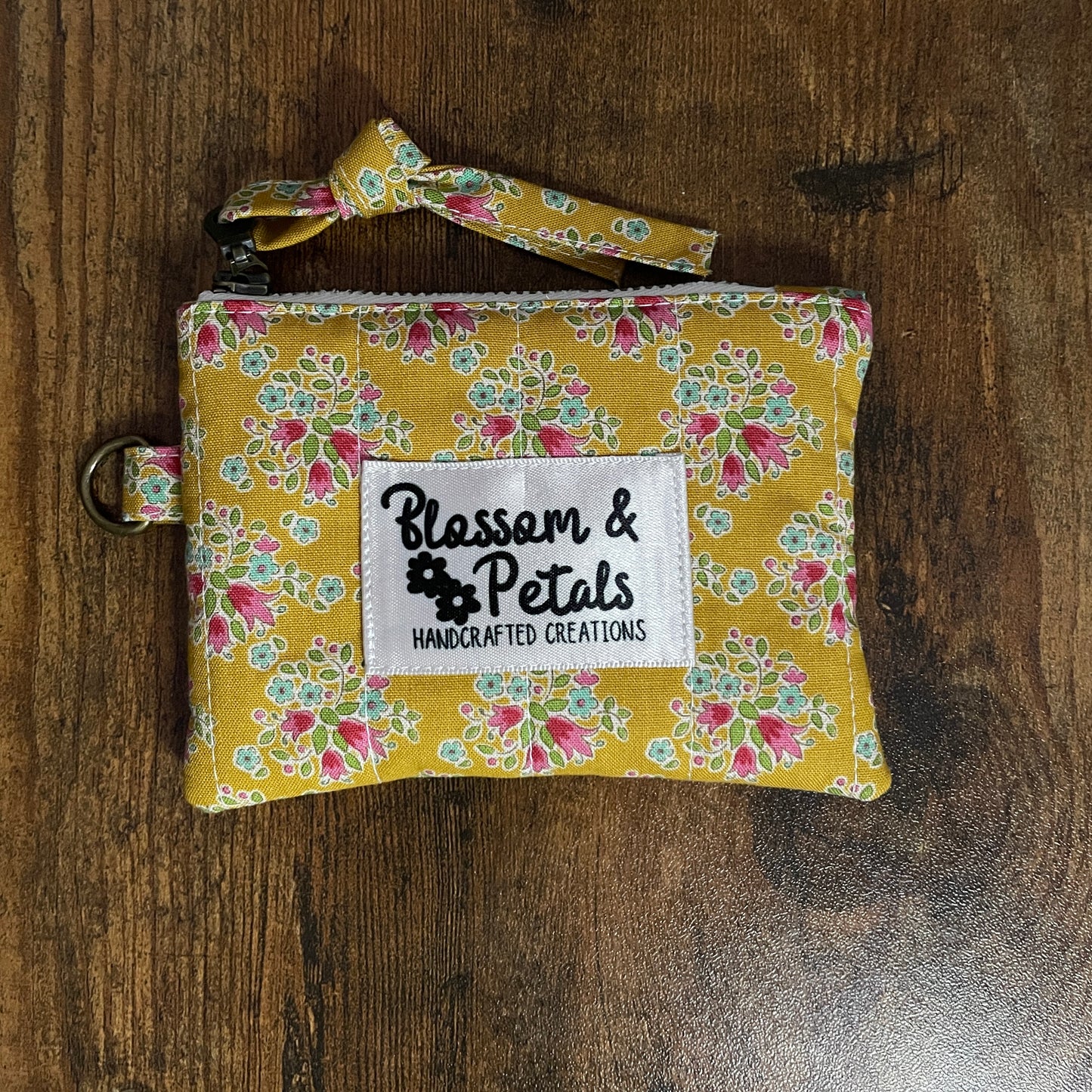 Handmade mustard floral quilted pouch with zip closure and wrist strap on wooden background