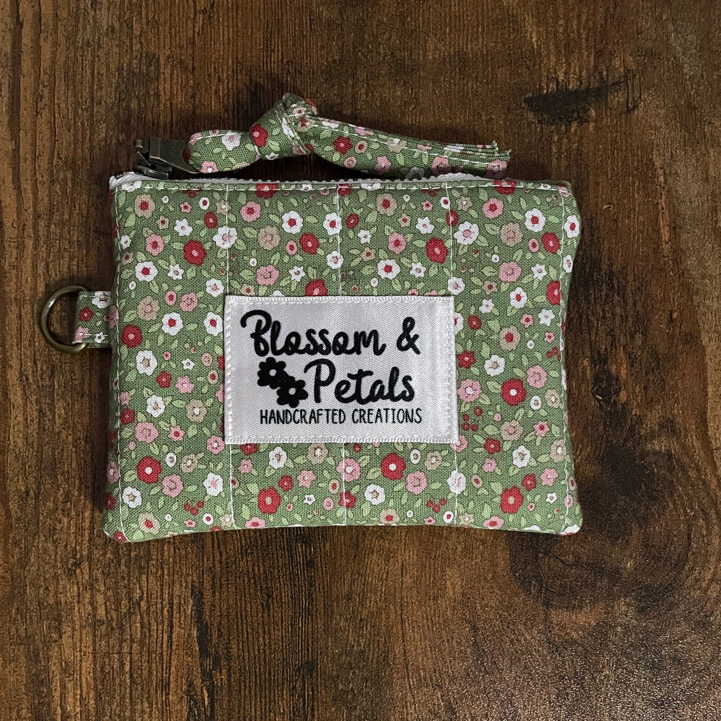 Handmade green floral quilted pouch with zip closure and wrist strap on wooden background