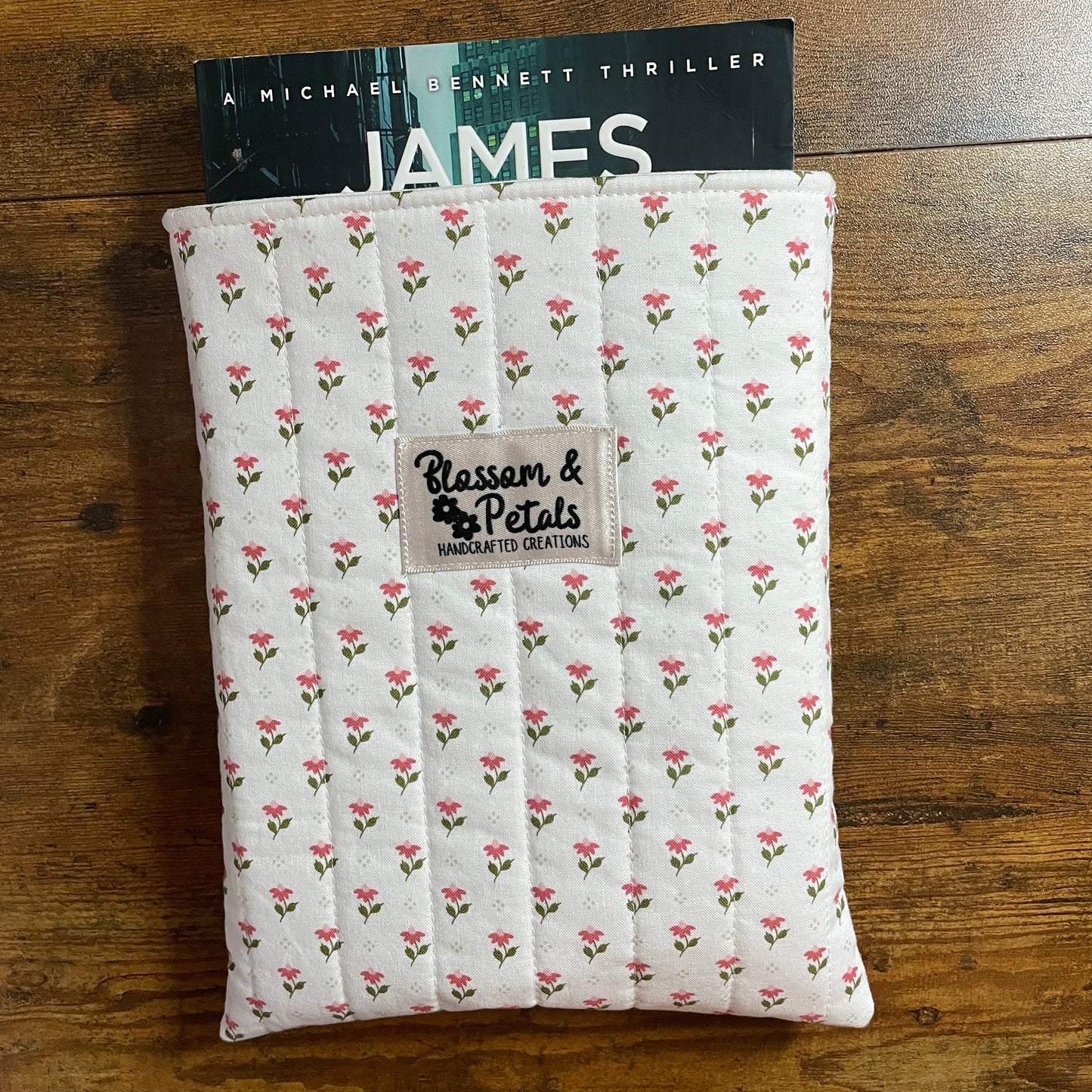 Handmade quilted white floral book sleeve with ditsy pink flower print and Blossom & Petals label, padded fabric book cover for books and journals.