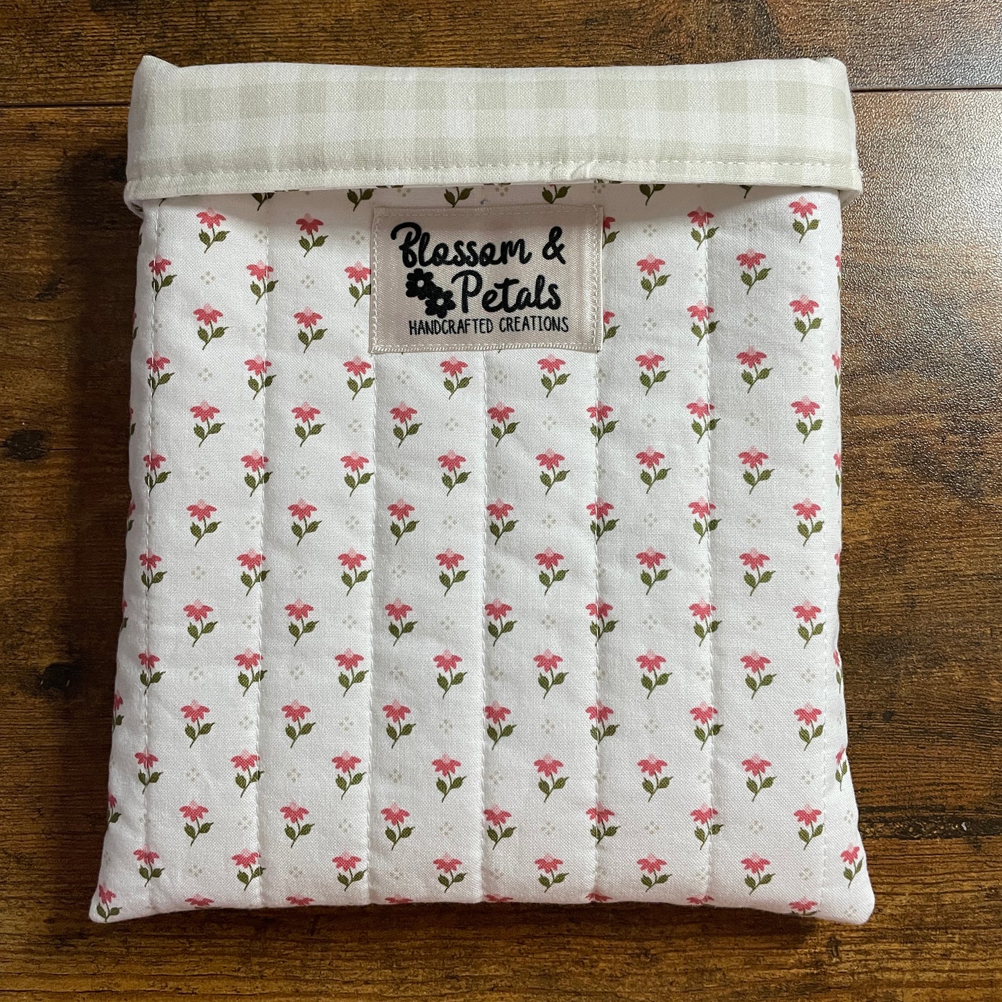 Handmade quilted white floral book sleeve with ditsy pink flower print and Blossom & Petals label, padded fabric book cover for books and journals.