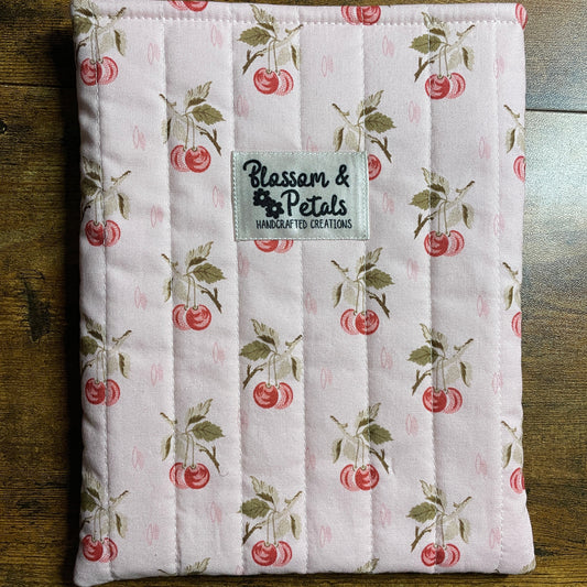 Handmade quilted pink book sleeve with cherry print fabric and Blossom & Petals label, padded fabric book cover for protecting books and journals.