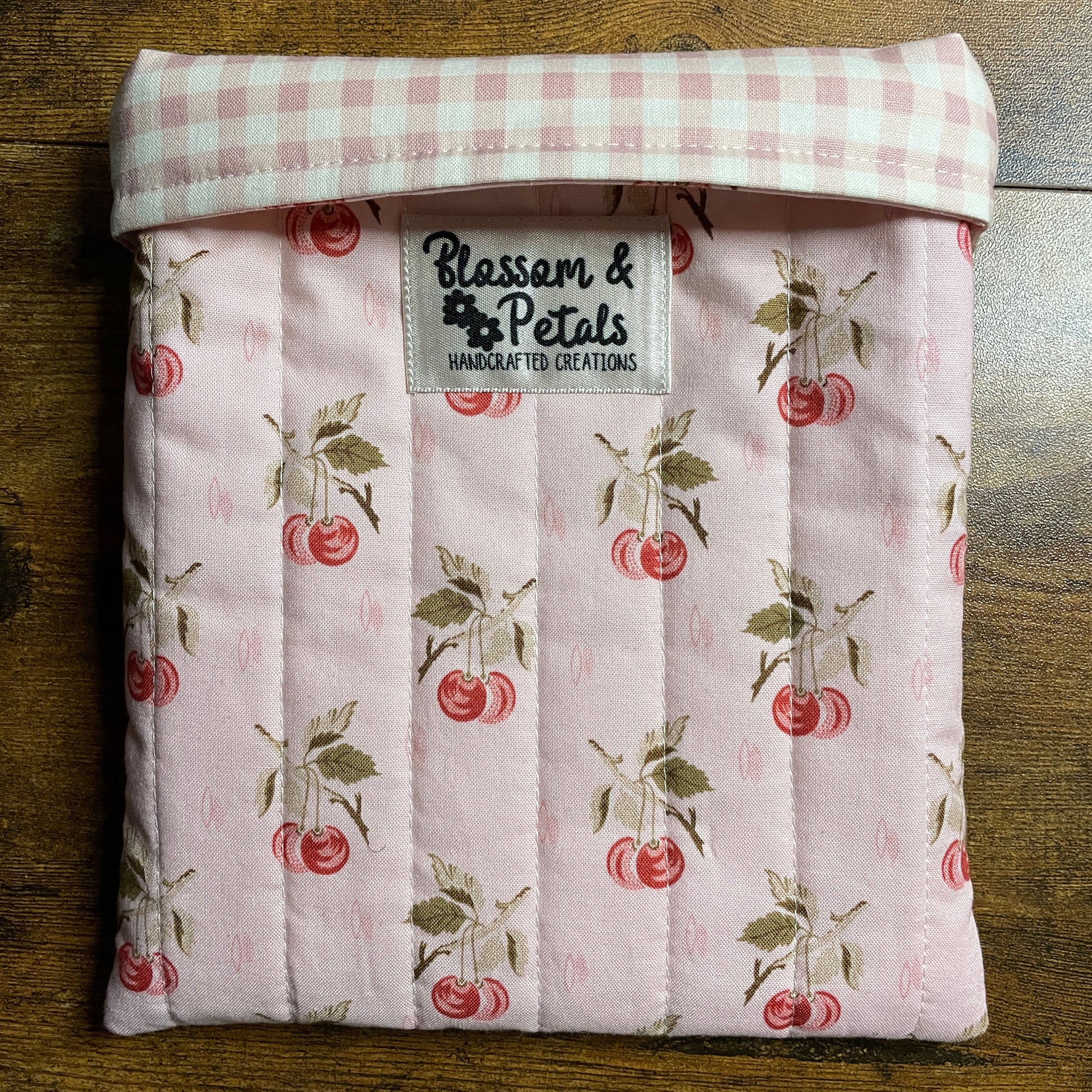 Handmade quilted pink book sleeve with cherry print fabric and Blossom & Petals label, padded fabric book cover for protecting books and journals.