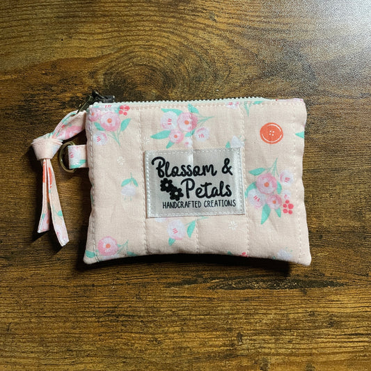 Handmade pink floral quilted zip pouch with Blossom & Petals label on wooden background.