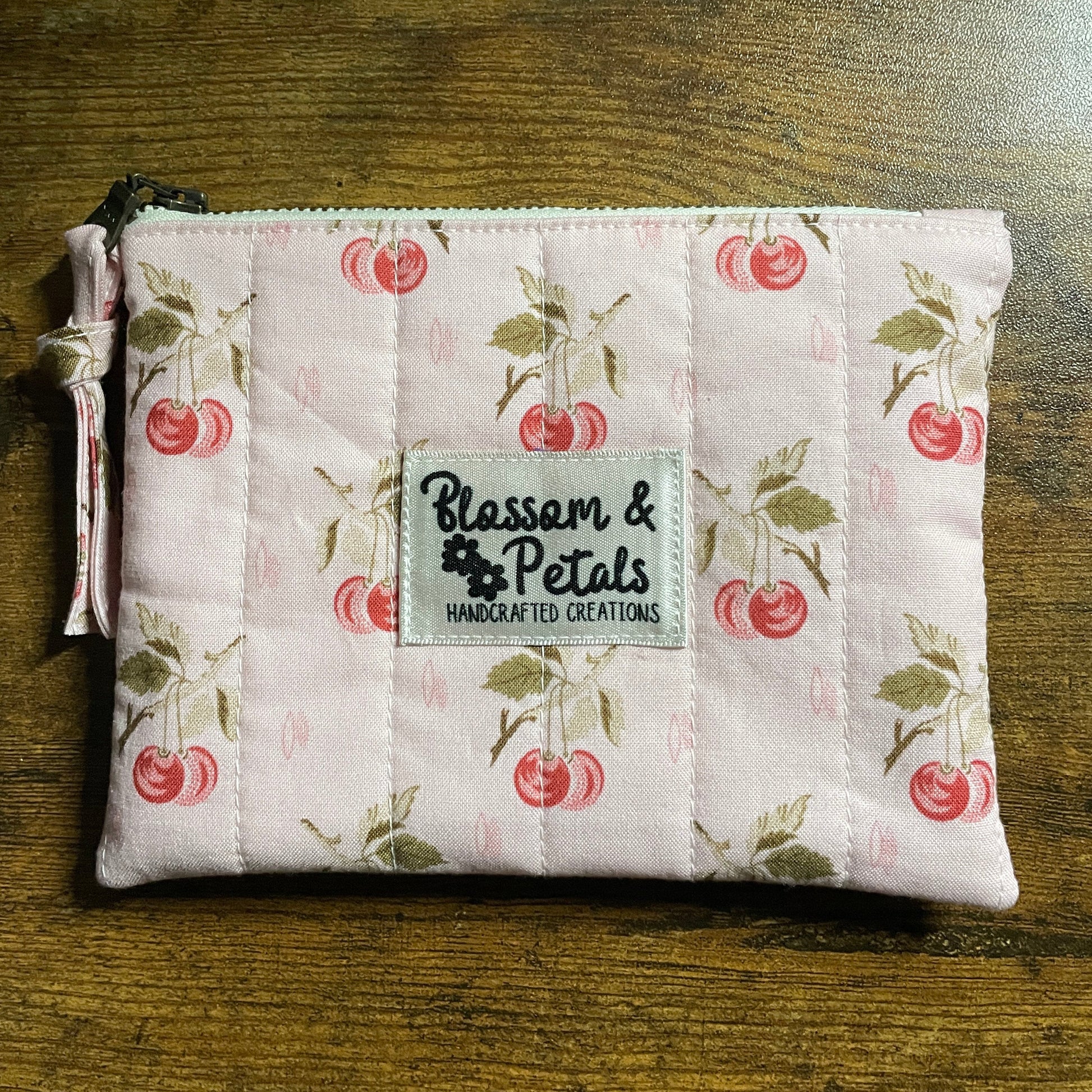 Handmade quilted zipper pouch in blush pink fabric with cherry print design and Blossom & Petals label.