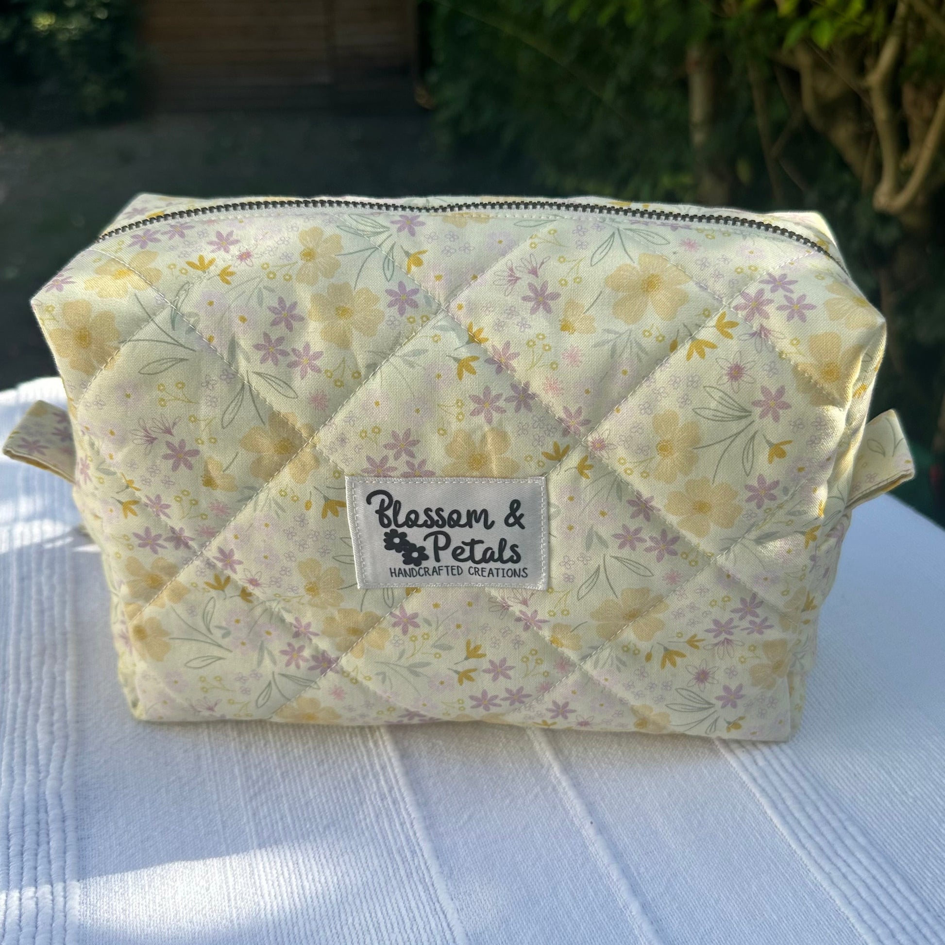 Handmade pastel floral quilted makeup bag with zipper closure, featuring yellow and lilac flower print, perfect for cosmetics and toiletries.