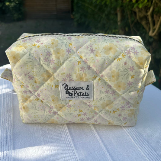 Handmade pastel floral quilted makeup bag with zipper closure, featuring yellow and lilac flower print, perfect for cosmetics and toiletries.