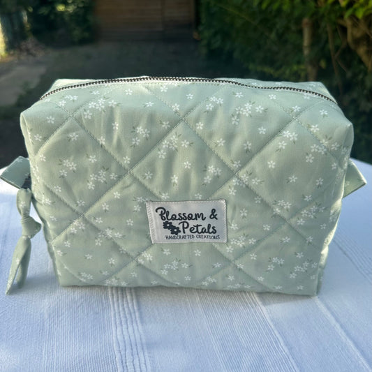 Handmade soft blue quilted makeup bag with white floral details, zipper closure, medium size for cosmetics and toiletries.