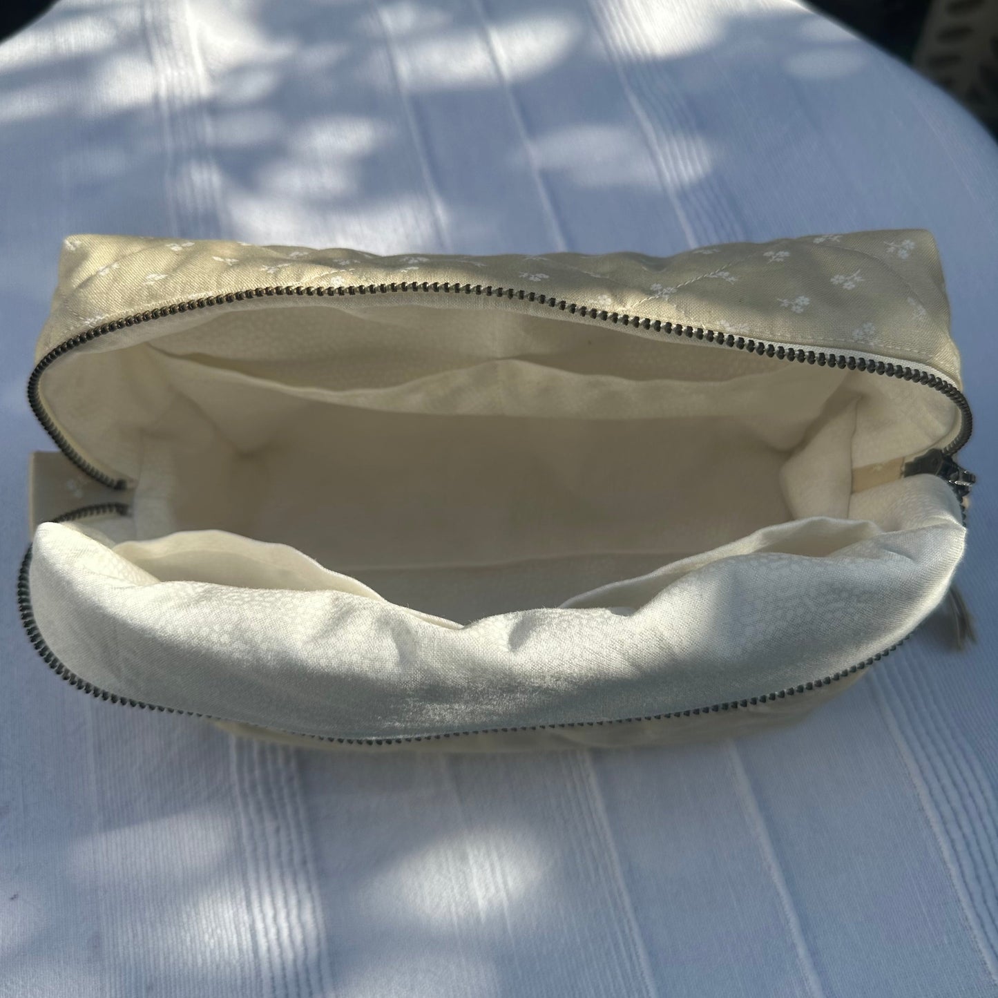 Open beige pouch with white interior on a textured white surface