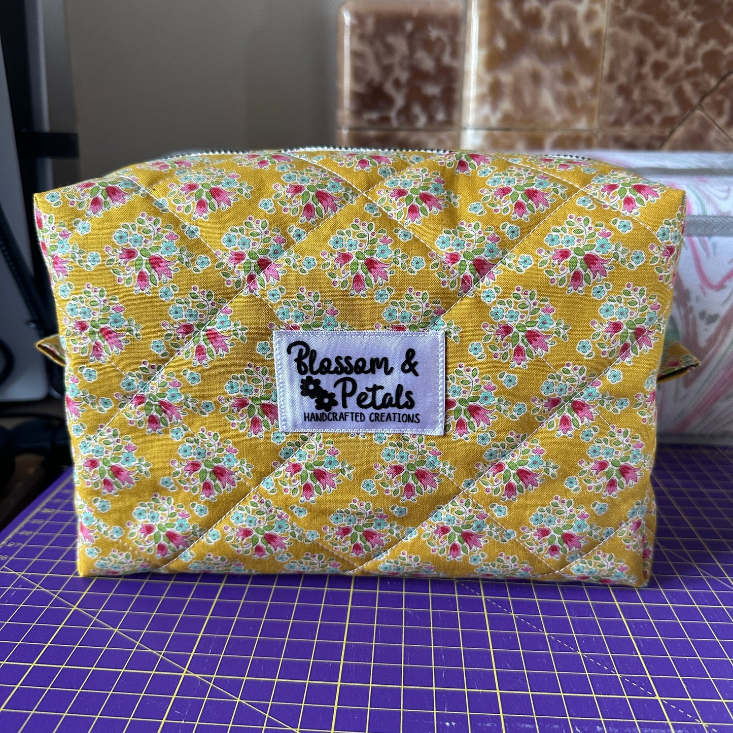 Handmade mustard yellow quilted makeup bag with floral cotton print, zippered cosmetic pouch for makeup, toiletries, and travel storage.