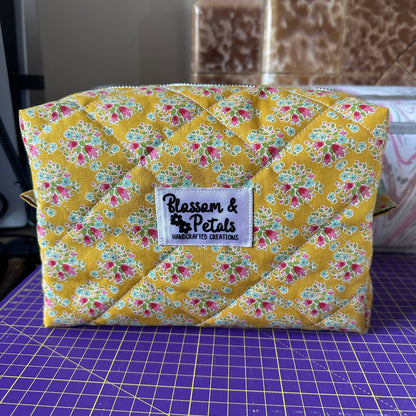 Handmade mustard yellow quilted makeup bag with floral cotton print, zippered cosmetic pouch for makeup, toiletries, and travel storage.